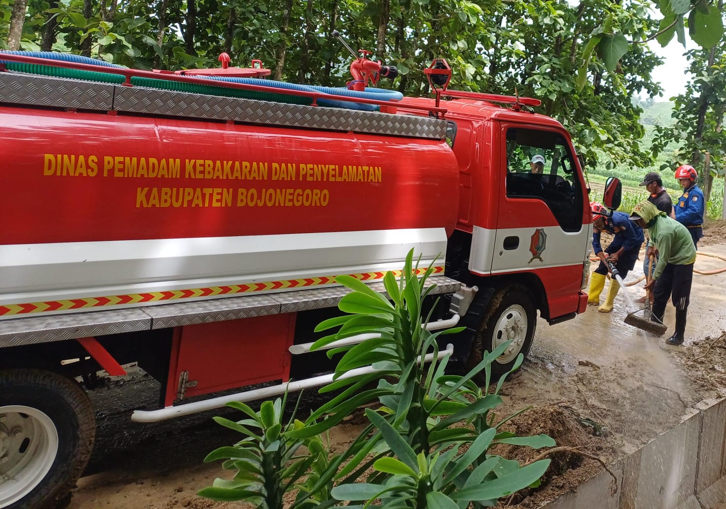 Damkar Pos Sekar Semprot Jalan Berlumpur di Desa Bareng